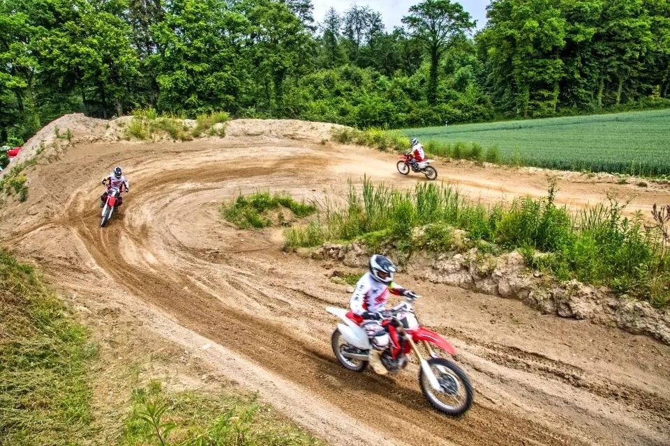 Action activities in Switzerland: three riders follow a winding sandy track between trees and a green field