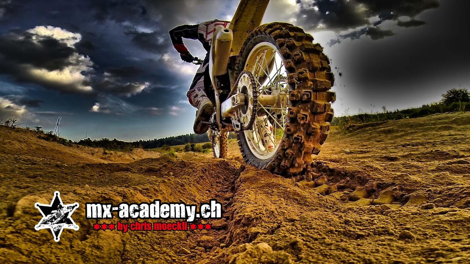 Best things to do in Switzerland for action: low view of a motocross rear wheel throwing sand under dark clouds