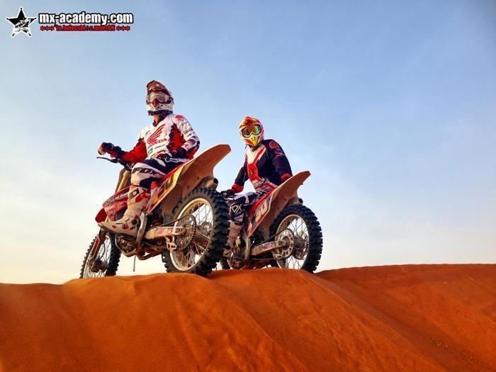 Book a desert ride: two riders sit on their bikes on the top of a red dune, with a clear sky behind them