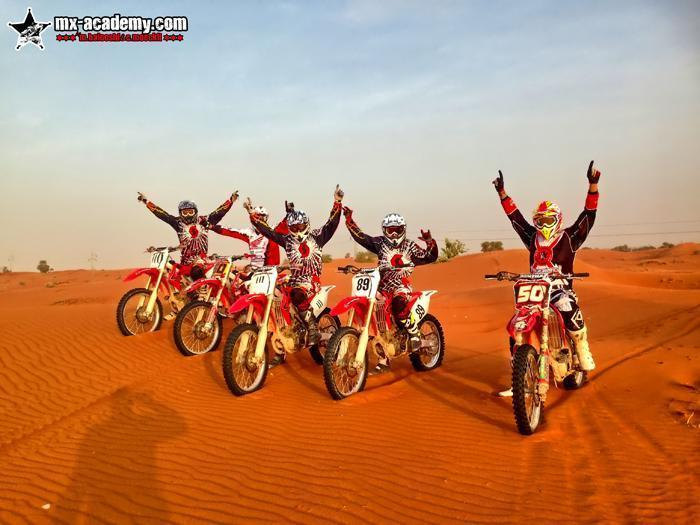 Book motocross in Dubai: a group of five riders on red bikes throws their arms up in the orange desert