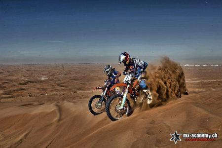 Contact MX-Academy Dubai for desert riding: two riders cross sand dunes, one bike throwing up a fountain of sand