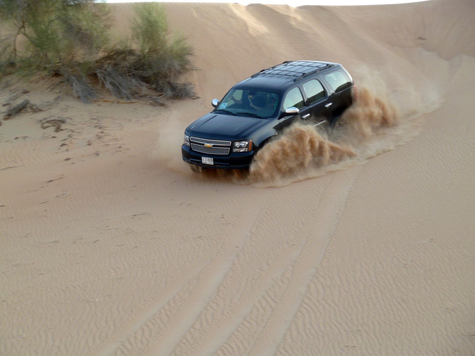 Desert drive Dubai: a black SUV slides down a sand slope and throws a spray of sand out behind it
