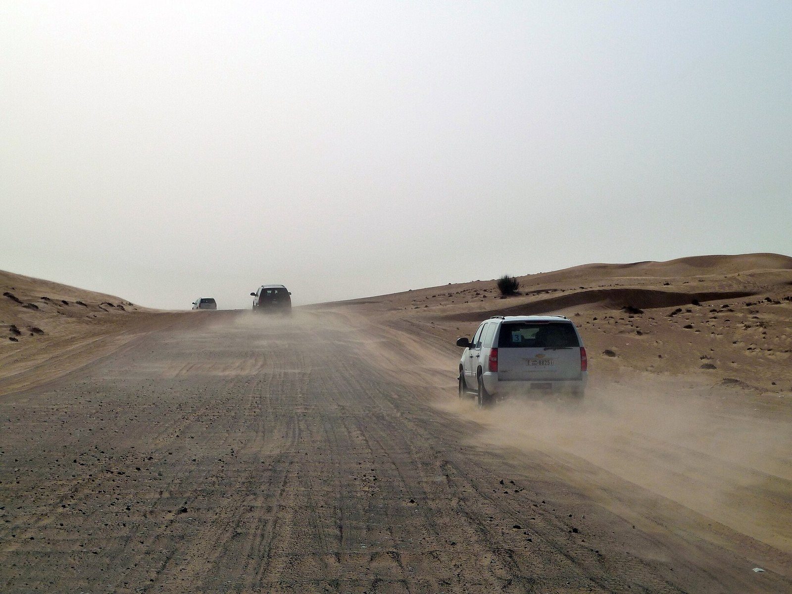 Desert safari Dubai: three four-wheel drives kick up dust on a wide sand track between low dunes