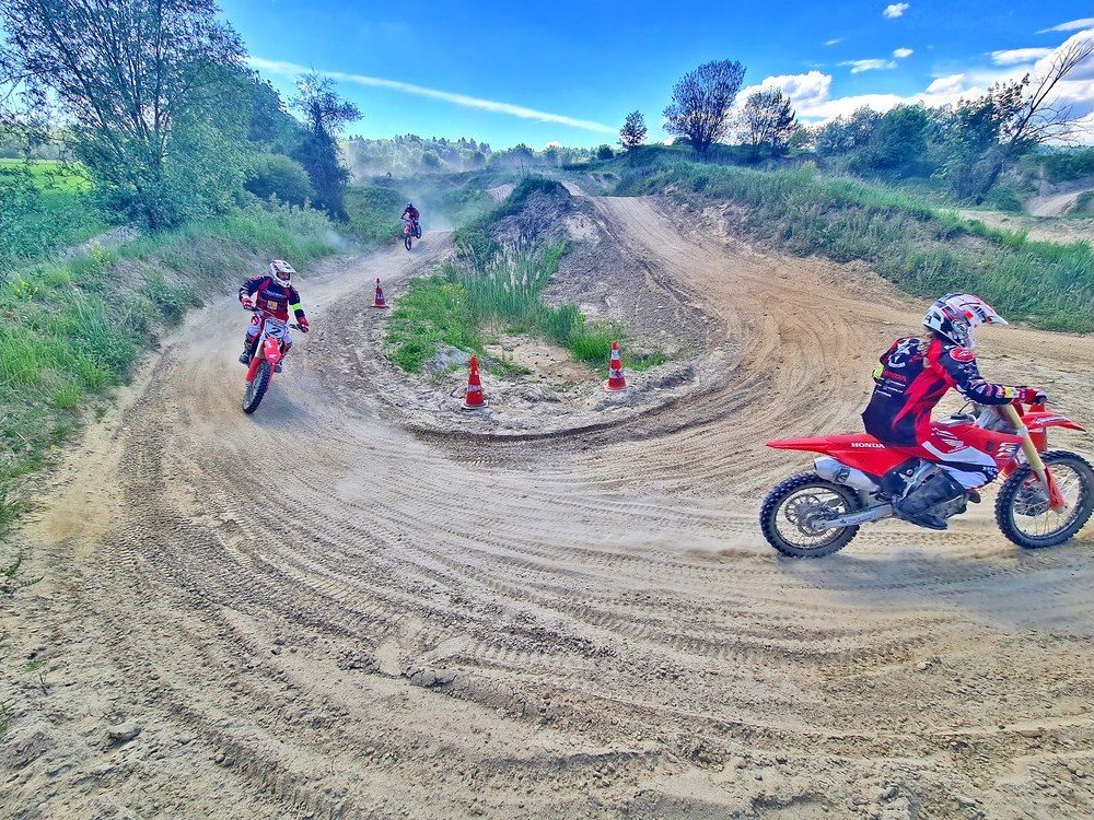 Dirt bike holiday packages: three riders on red Honda bikes take sandy bends marked with orange cones