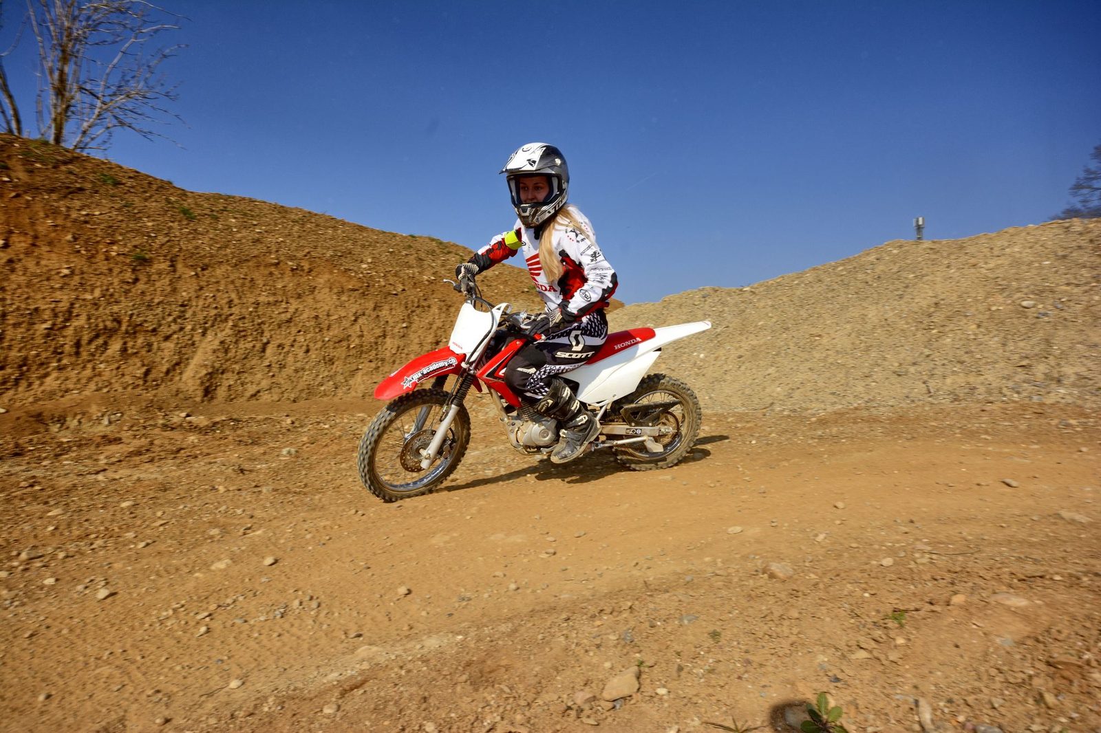 Dirt bike holidays for beginners: a young woman on a red and white Honda rides a dirt path between earth banks