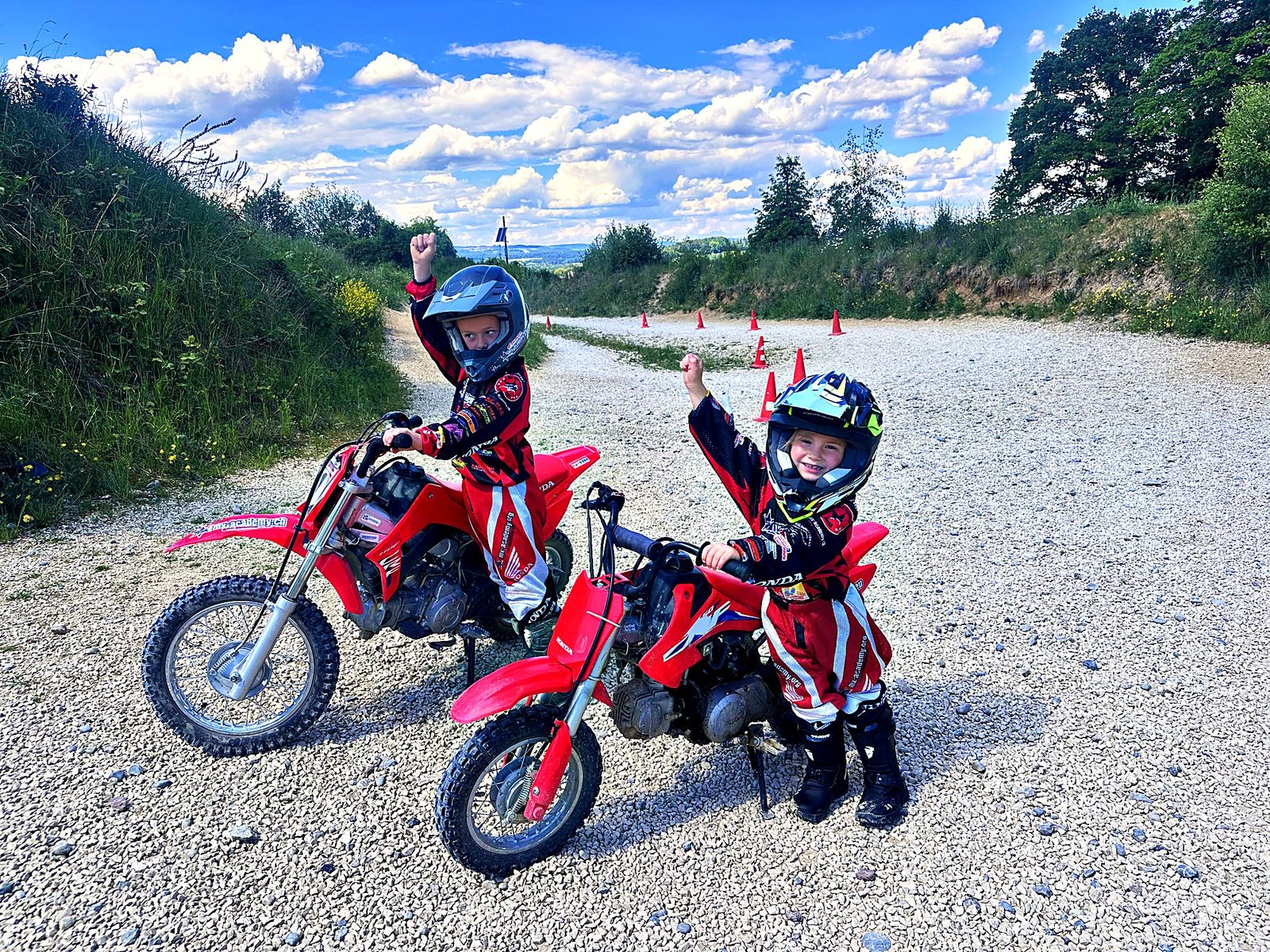 Dirt bike holidays with kids: two young children with small red Honda bikes raise their fists on a gravel track