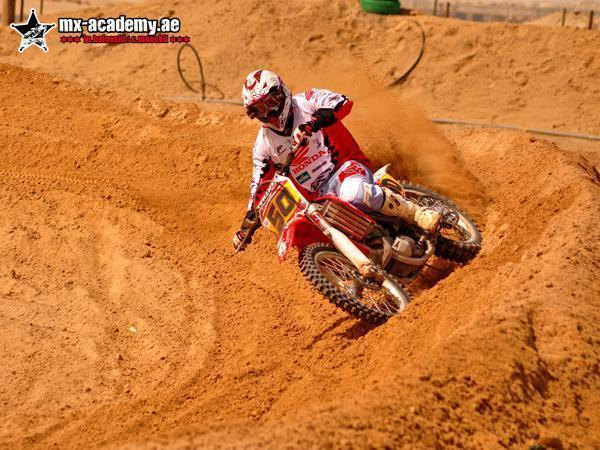 Dirt bike training in Dubai: rider number 50 steers a red Honda through a deep rutted berm of orange sand