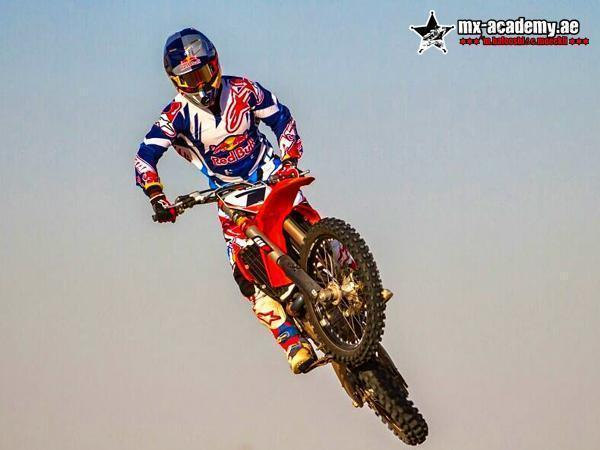 Dirt bike UAE: a rider in blue and white Red Bull kit takes a red Honda high into a pale, hazy sky