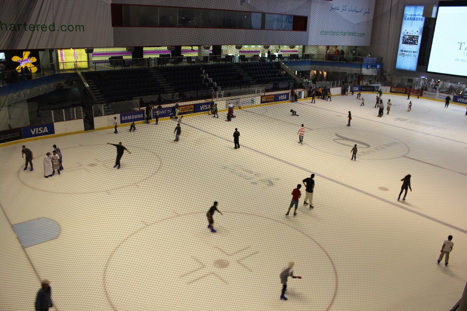 Dubai activities indoors: skaters glide across a large ice rink seen from above, with stands and big screens