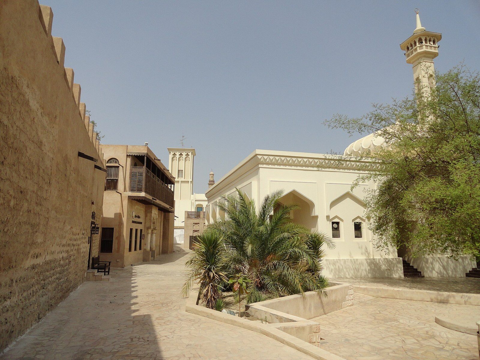Dubai city tour on foot: a quiet lane with sand-coloured walls, a wind tower and a white mosque with a minaret
