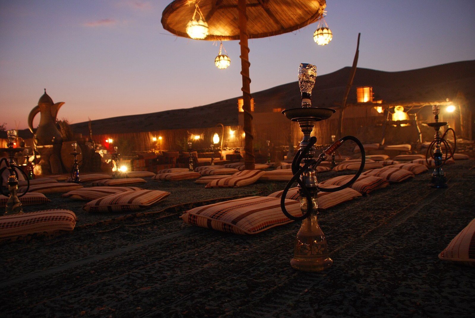 Dubai desert tours: a desert camp at dusk with floor cushions, shisha pipes and glowing lanterns
