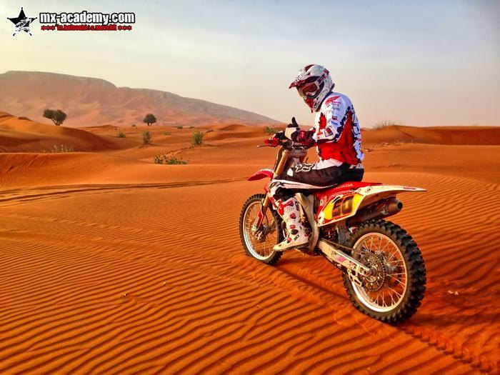Dubai dunes on a motorbike: a rider in red and white gear sits on a red motocross bike on rippled sand