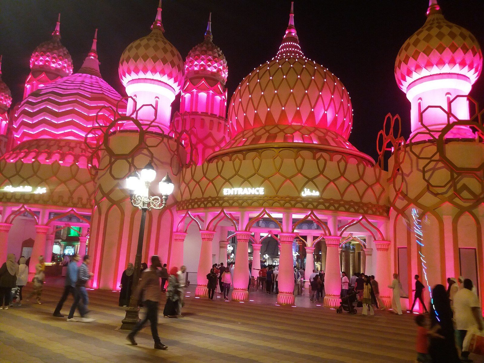 Dubai evenings out: the pink-lit domes of the Global Village entrance at night, with visitors walking by
