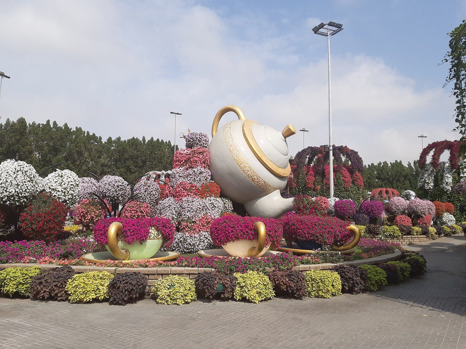 Dubai itinerary in winter: a giant white teapot and cups among colourful flower beds and flower-covered arches