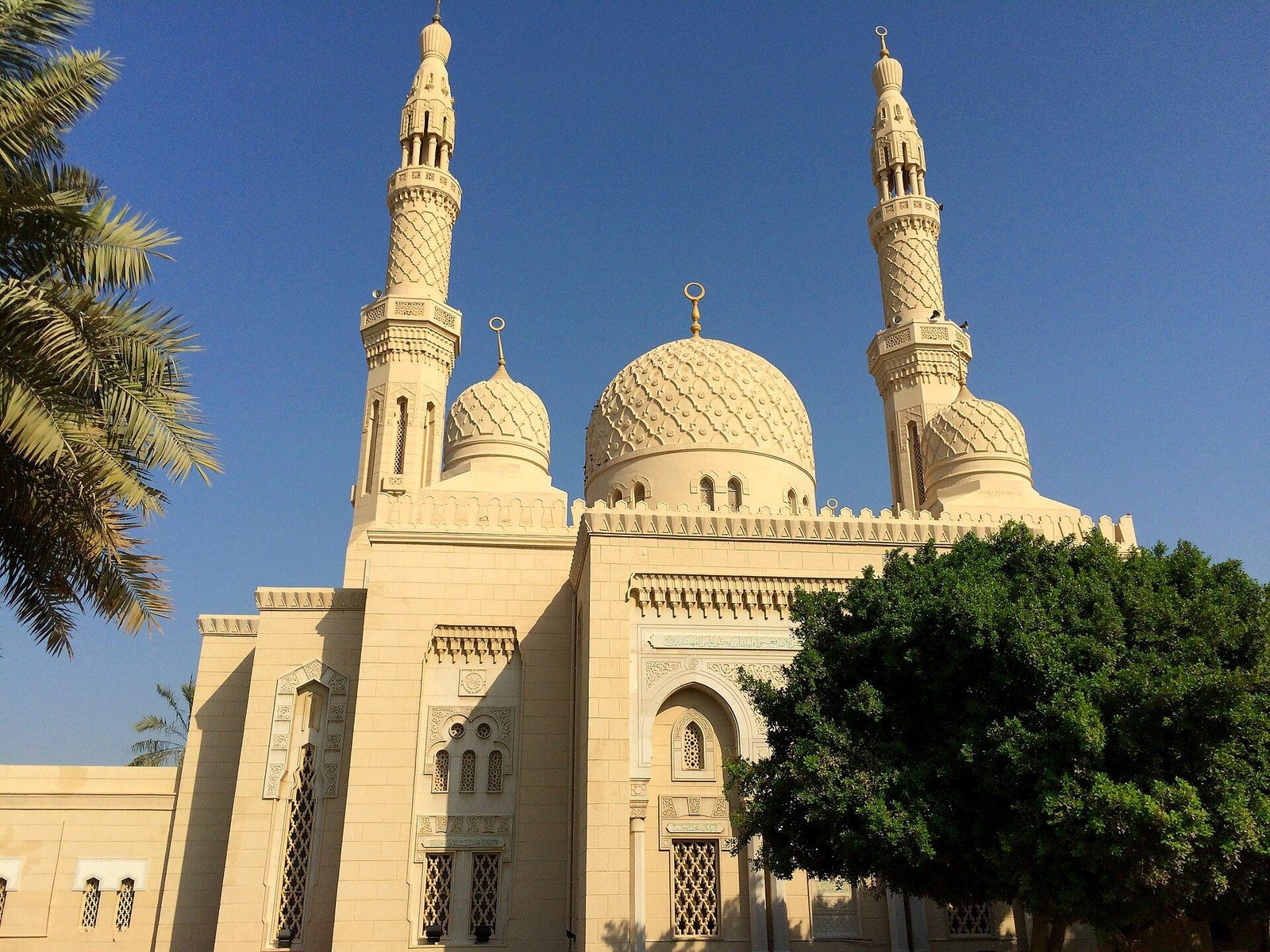 Dubai landmarks: the Jumeirah Mosque with two minarets and carved domes in pale stone under a blue sky