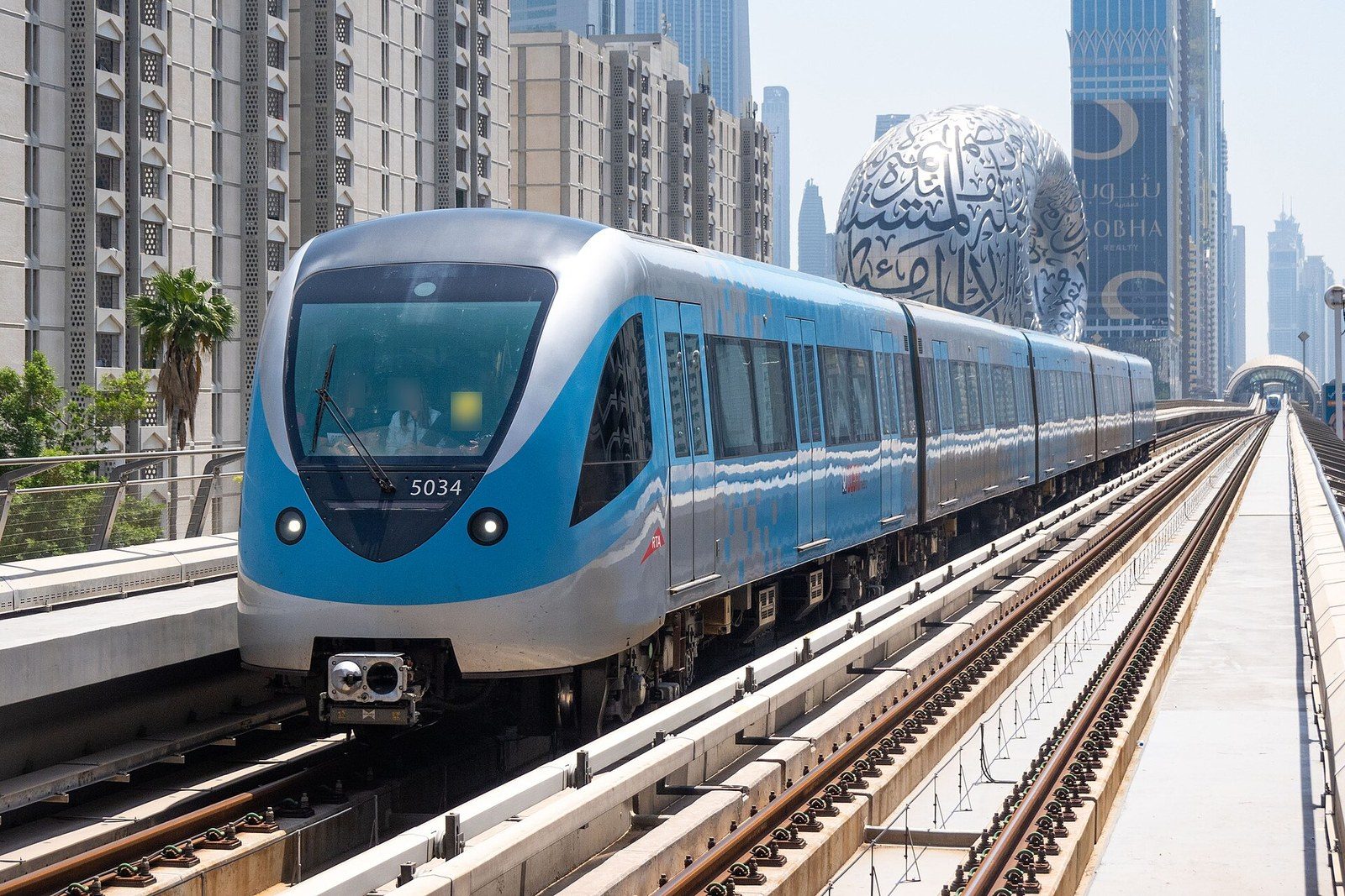 Dubai neighbourhoods by metro: a blue and white train on an elevated track, with the Museum of the Future behind