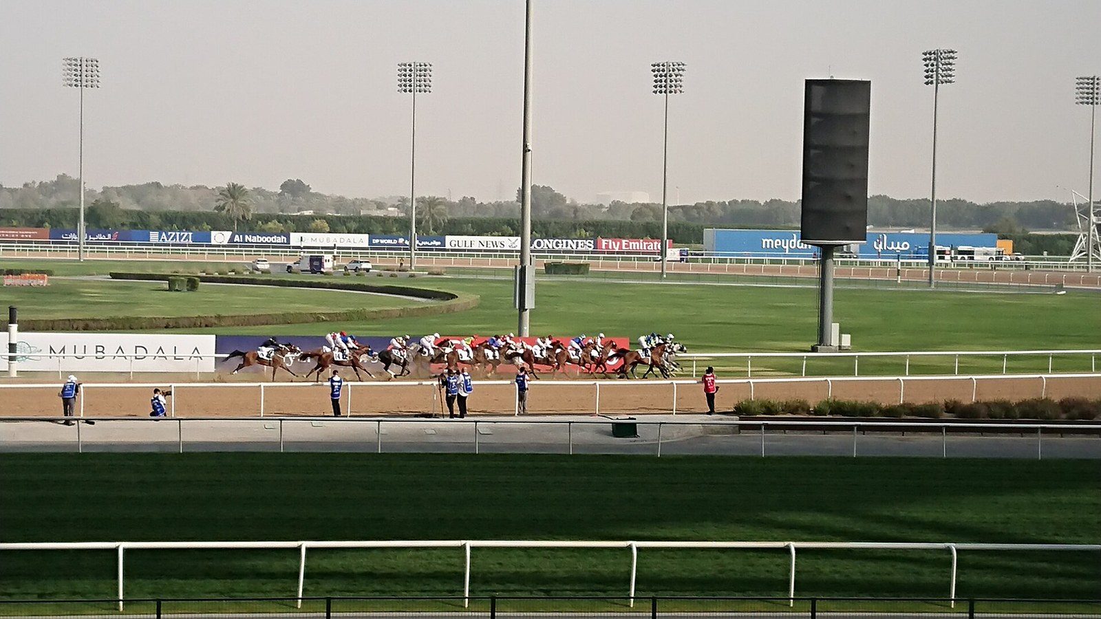 Dubai racing on horseback: a field of horses and jockeys gallops along a sandy track past advertising boards