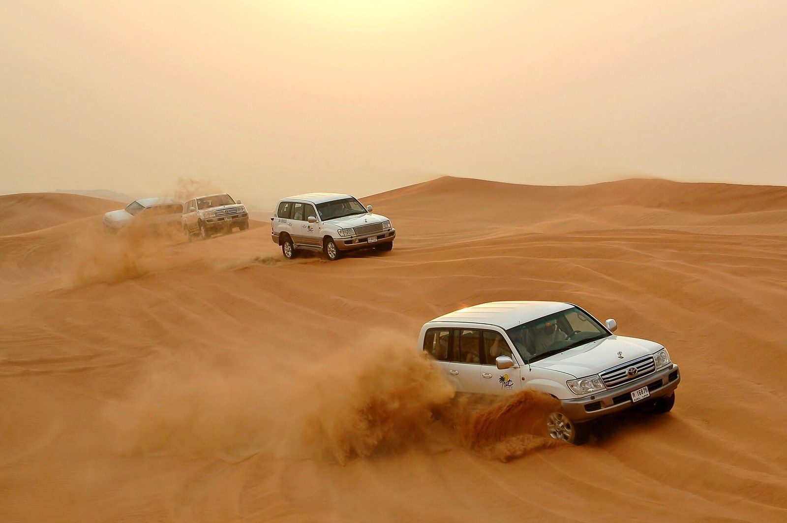 Dune bashing in Dubai: three white four-wheel drives race over orange sand and throw up clouds of dust