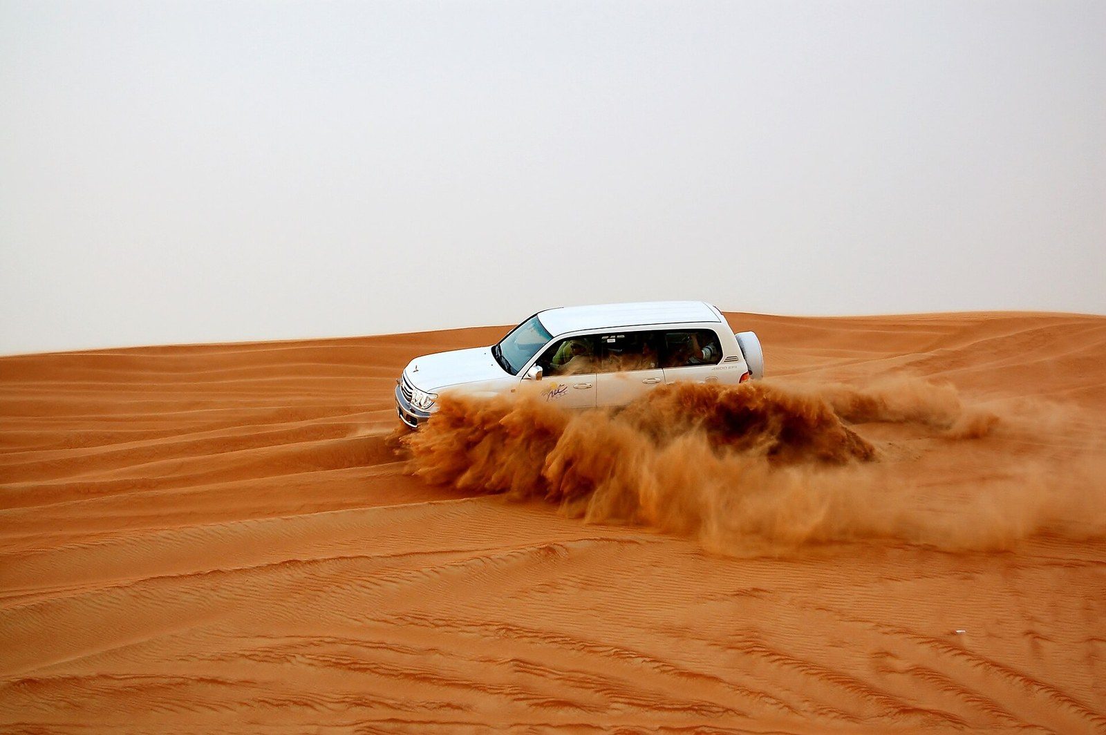 Dune bashing in Dubai: a white SUV slides along a sand slope and sends a wave of orange sand into the air