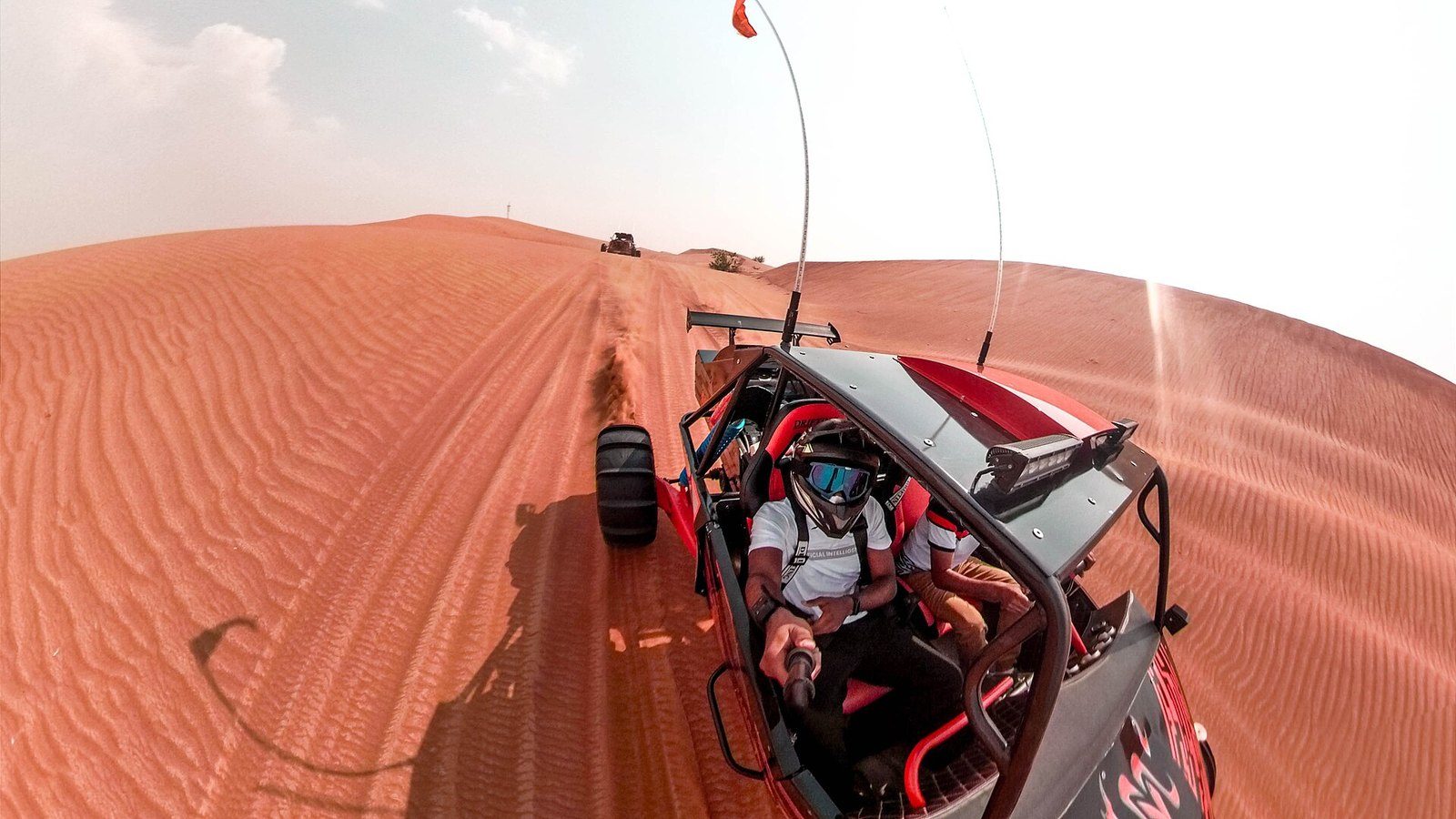 Dune buggy in Dubai: a red buggy with roll cage and whip flags crosses red dunes, its driver in helmet and goggles