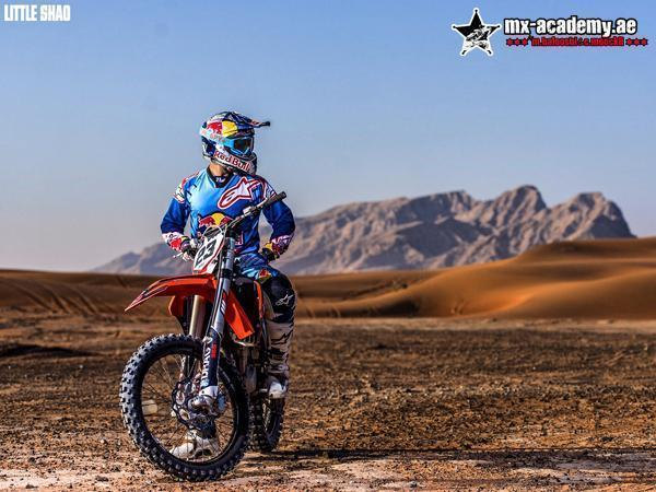 Enduro in Dubai: a rider in blue Red Bull gear waits on an orange bike, a stony plain and mountains behind