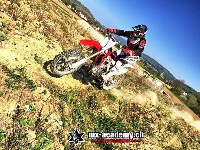 Enduro travel: a rider on a red and white bike on a steep, dusty hillside with a village far below
