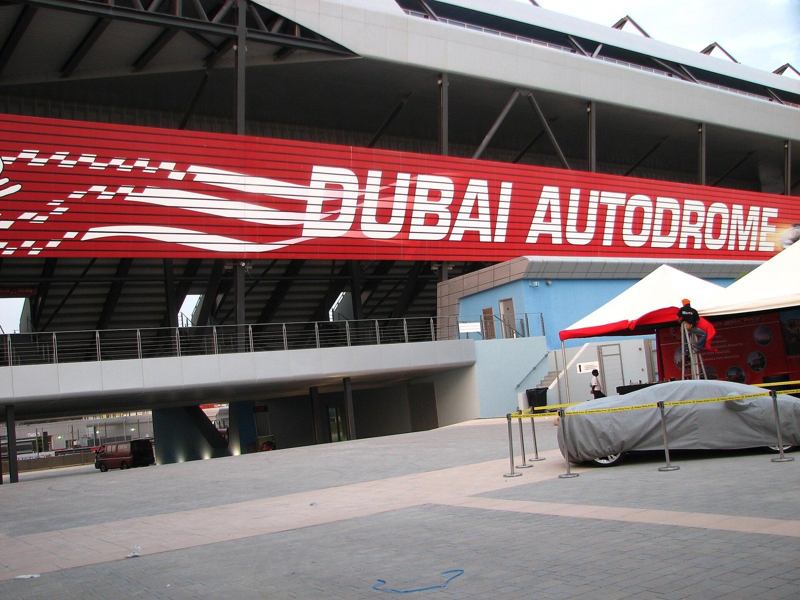 Go-karting in Dubai: a covered grandstand with a large red-and-white sign above a paved plaza and a covered car