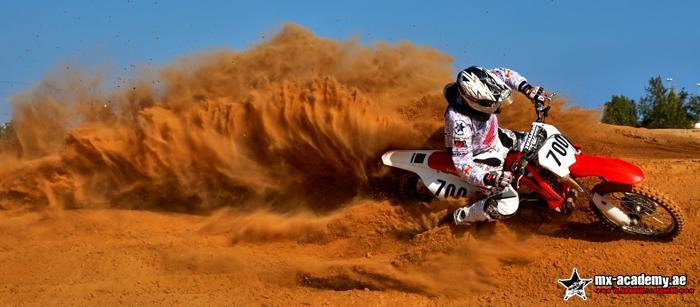 Karting in Dubai and beyond: a rider on a red motocross bike with number 700 throws up a wall of orange sand