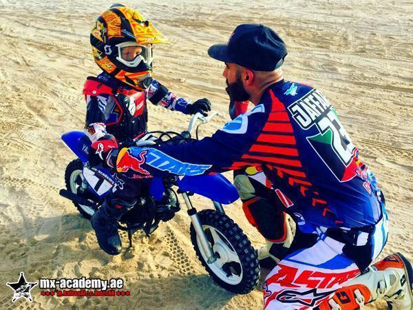 Kids motocross Dubai: bearded coach in a black cap explains something to a little rider on a blue kids' bike