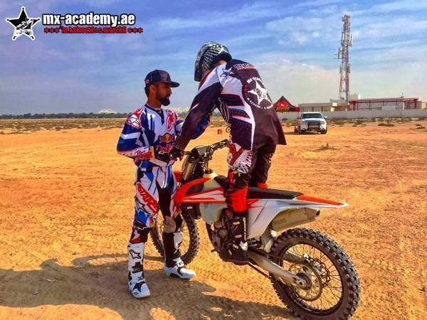 Motocross for kids in Dubai: coach in blue and white gear helps a beginner stand on the pegs of an orange KTM