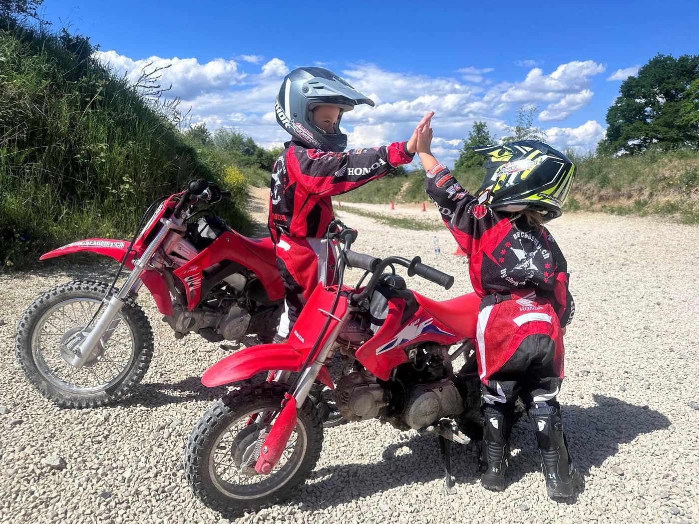 Motocross holiday in Switzerland: two children on red Honda kids’ bikes give each other a high five on gravel