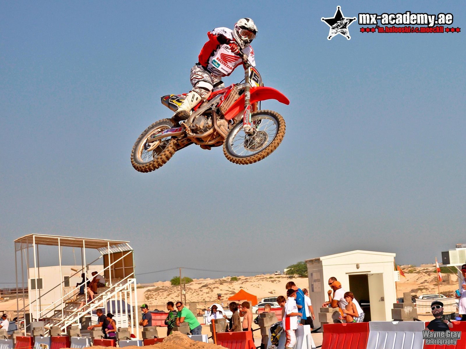 Motocross in Dubai: a Honda rider in white and red flies high over the track while spectators watch from below