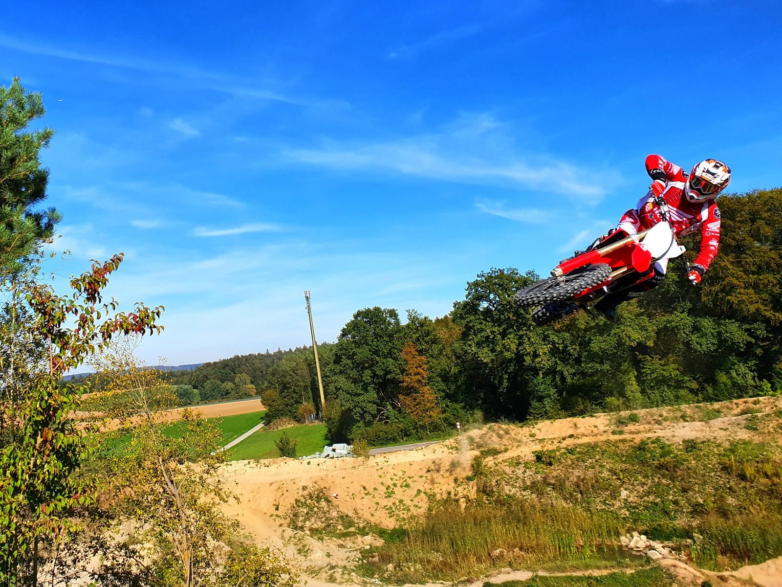 Motocross in Switzerland: rider jumping a Honda against a blue sky above green countryside