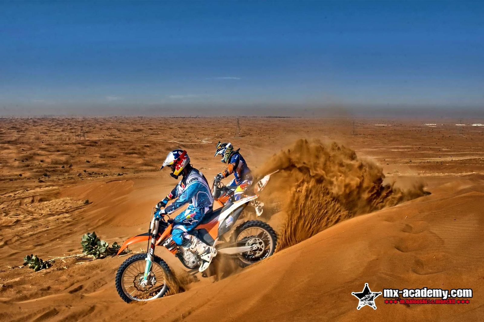 Motocross in the dunes of Dubai: two riders on motocross bikes with sand spraying up behind them