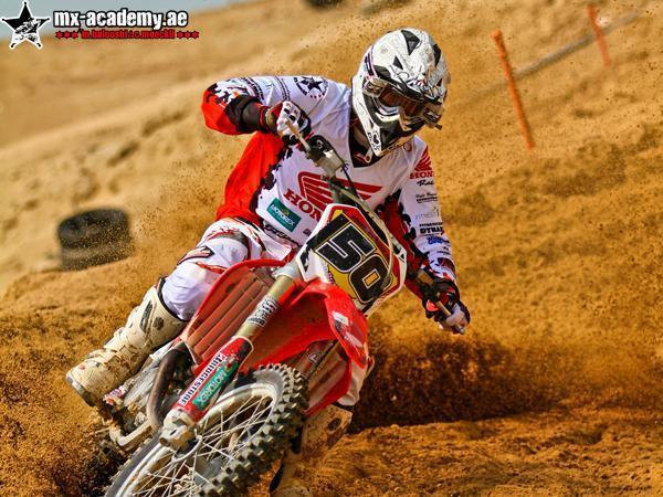 Motocross lessons in Dubai: rider number 50 on a red Honda throws up sand in a turn, a tyre and poles behind