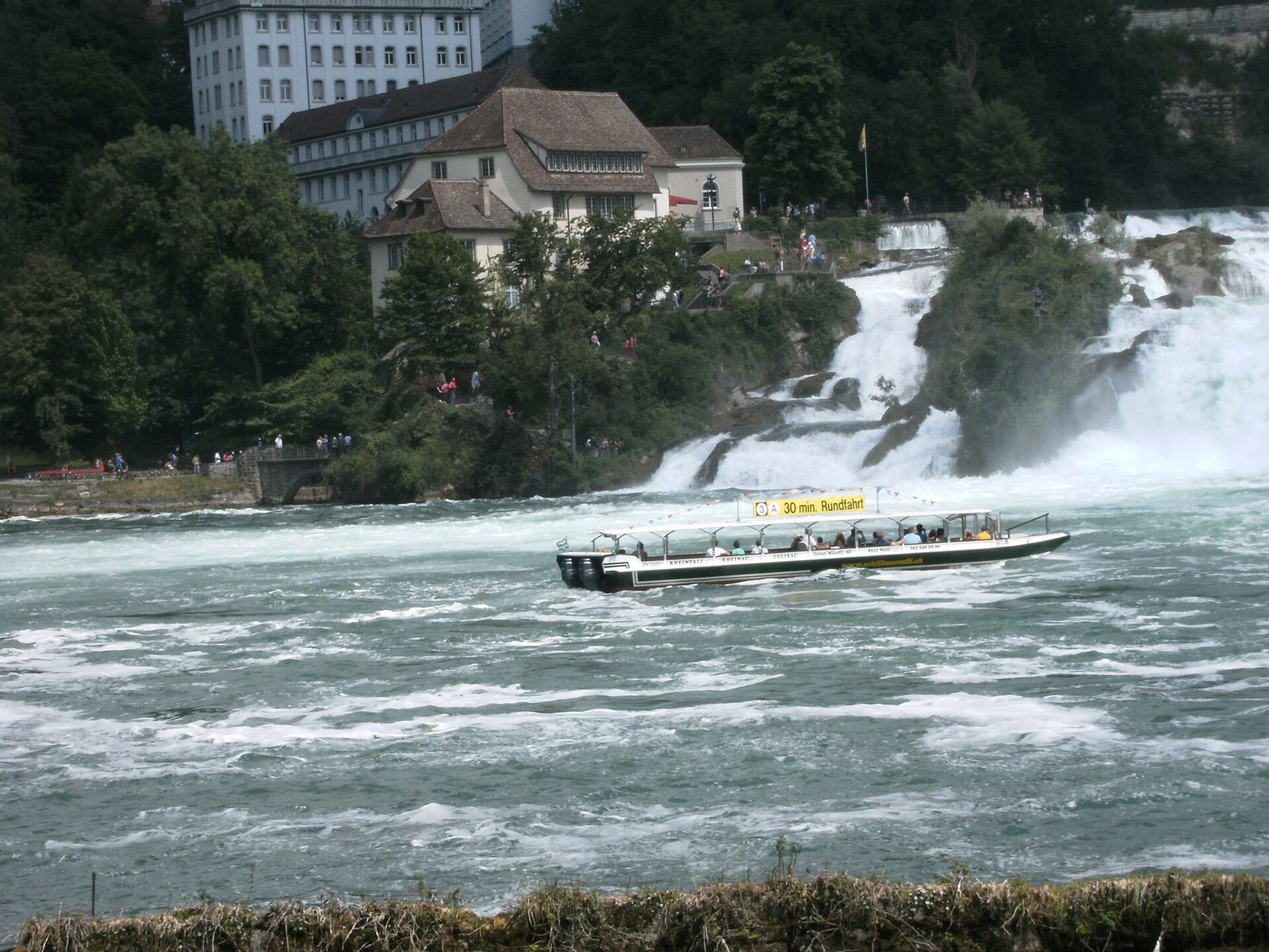 Motocross trip to Switzerland plus sightseeing: a tour boat with passengers crosses the foaming basin of the Rhine Falls