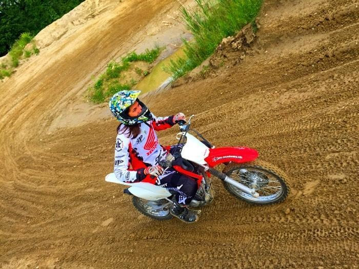 Motocross trip to Switzerland: a rider with a colourful helmet leans a red and white Honda into a sandy banked bend