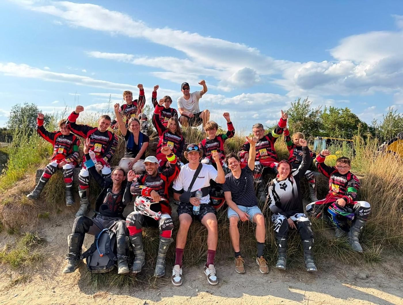 Motocross vacations with friends: a cheerful group, many in riding gear, raises their fists on a grassy bank