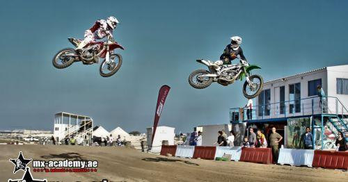 Motor racing in Dubai on two wheels: two motocross riders jump side by side as spectators watch beside the track