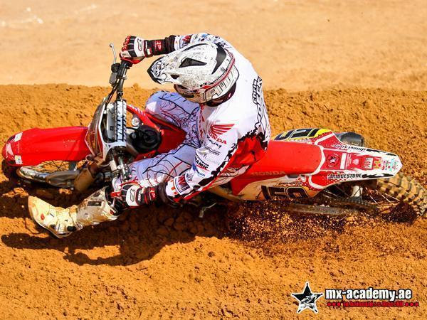 Off-road motorcycle course: rider in white Honda gear lies low over the bike in a tight turn, seen from above