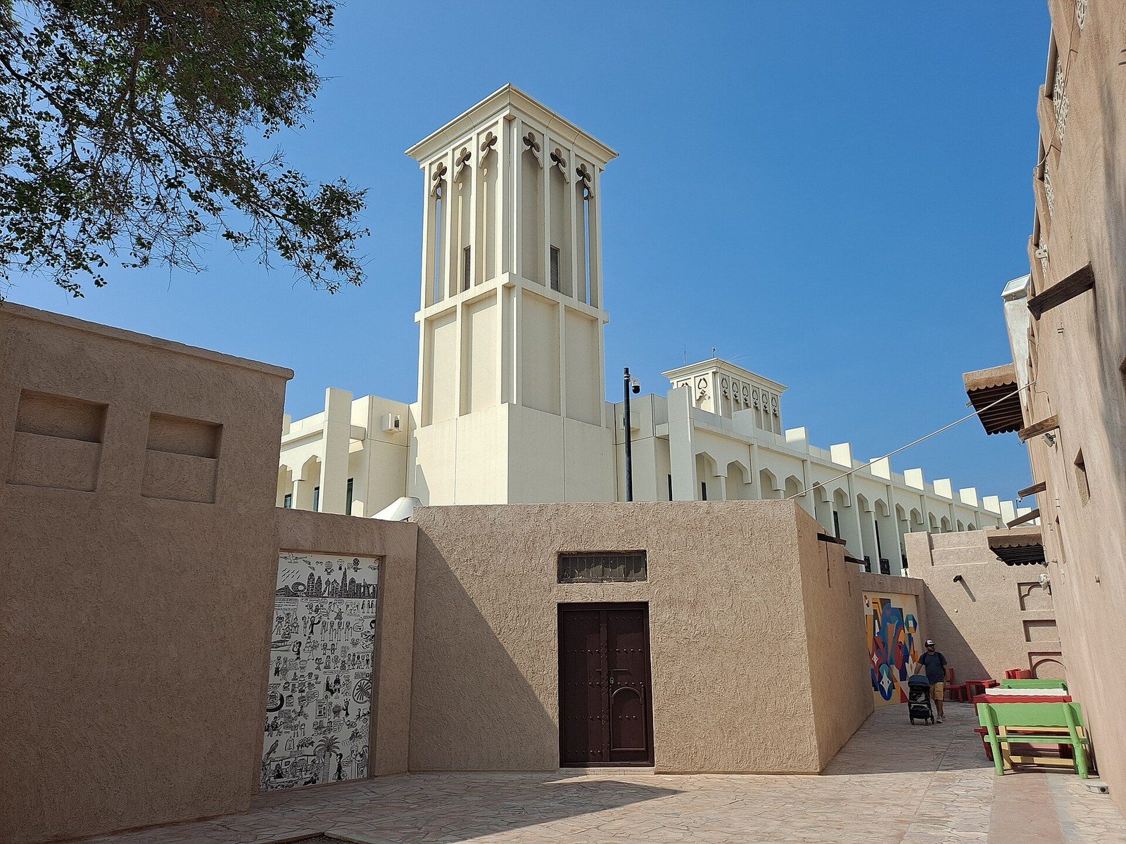 Old Dubai: a white wind tower above sand-coloured courtyard walls and a dark wooden door in Al Fahidi