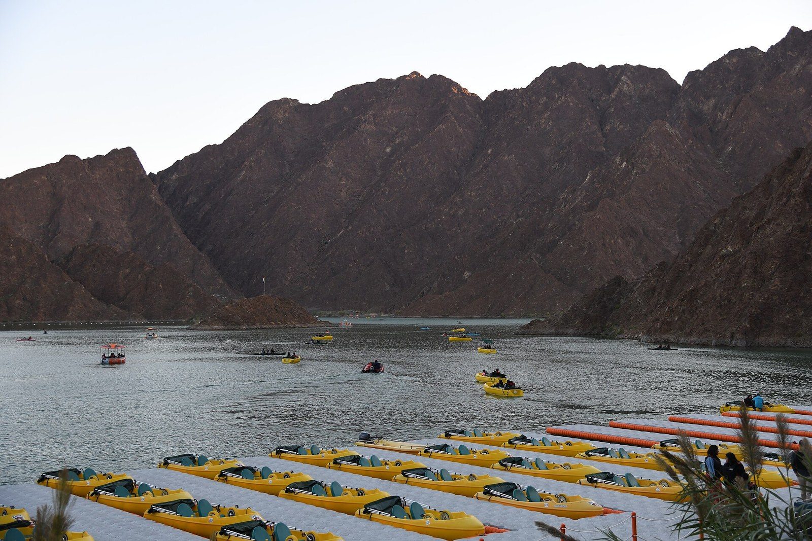 Outdoor activities in Dubai: rows of yellow kayaks and pedal boats on a lake between rocky brown mountains