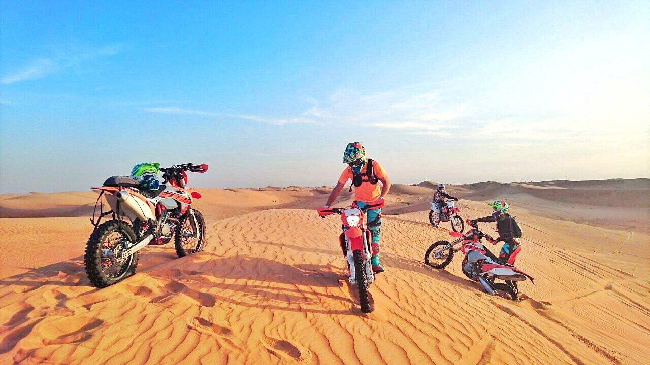 Quad biking in Dubai versus motorbikes: four riders in helmets with motocross bikes on rippled orange dunes
