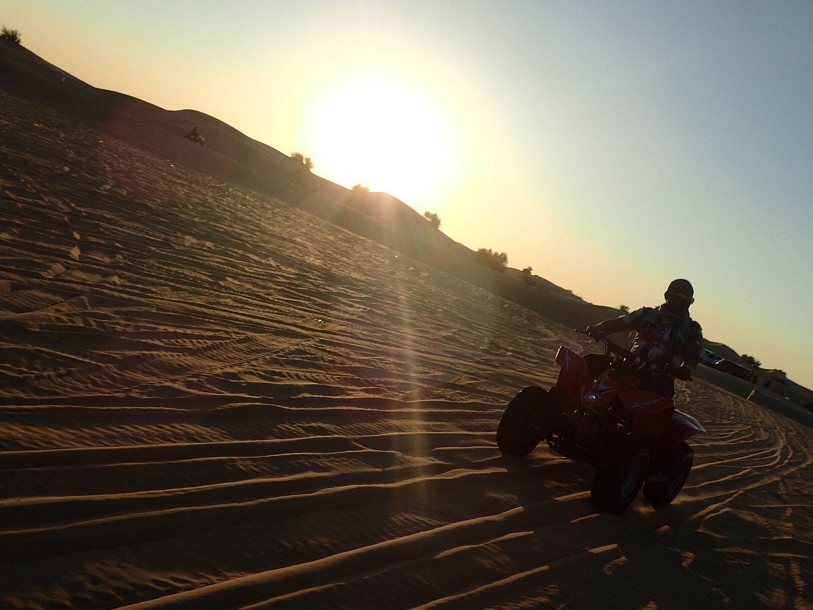 Quad biking in the desert: a rider on a quad bike climbs a dune slope while the low sun shines over the ridge