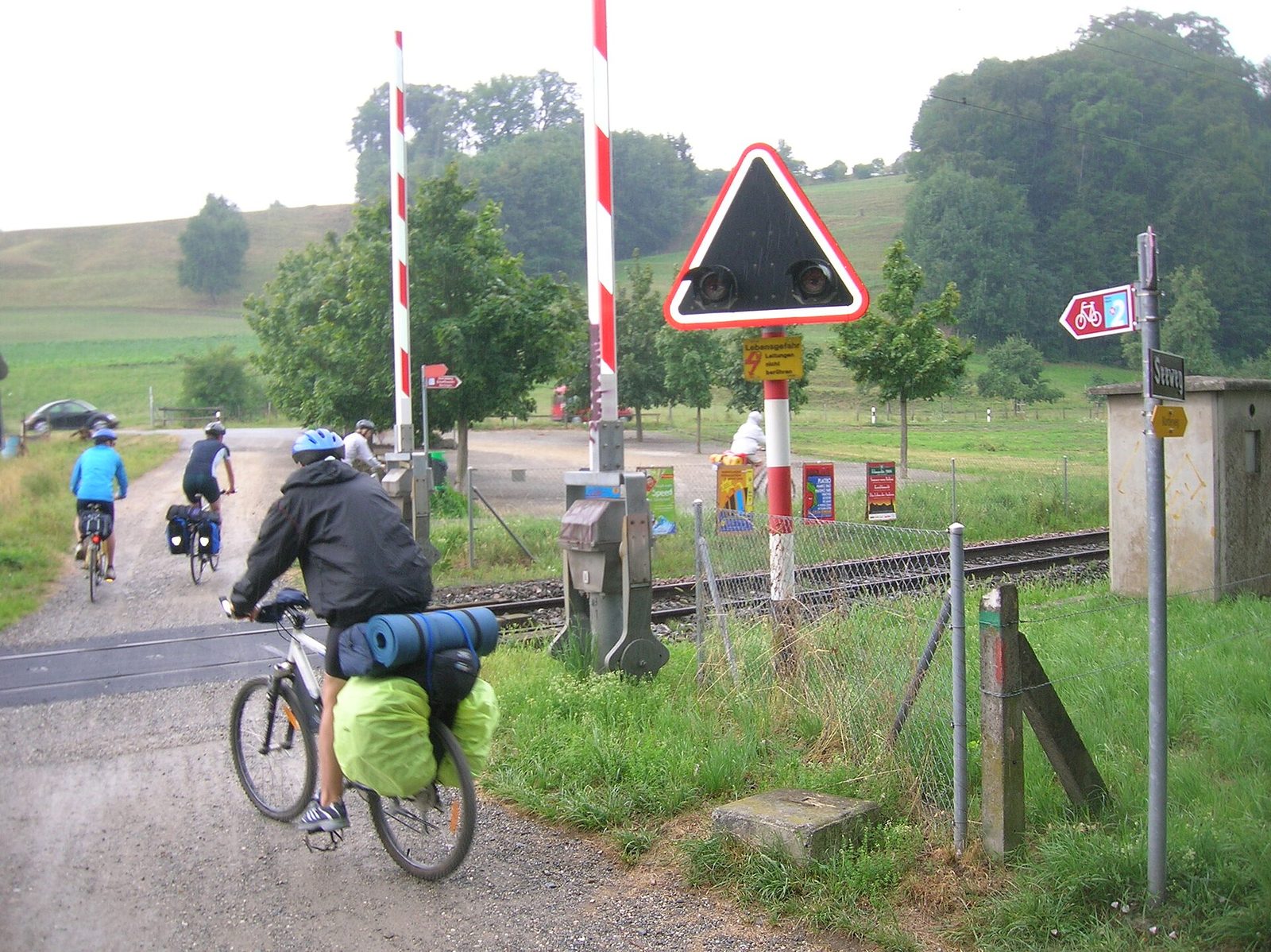 Switzerland activities by bike: cyclists with panniers cross a railway line beside a route 2 cycle sign