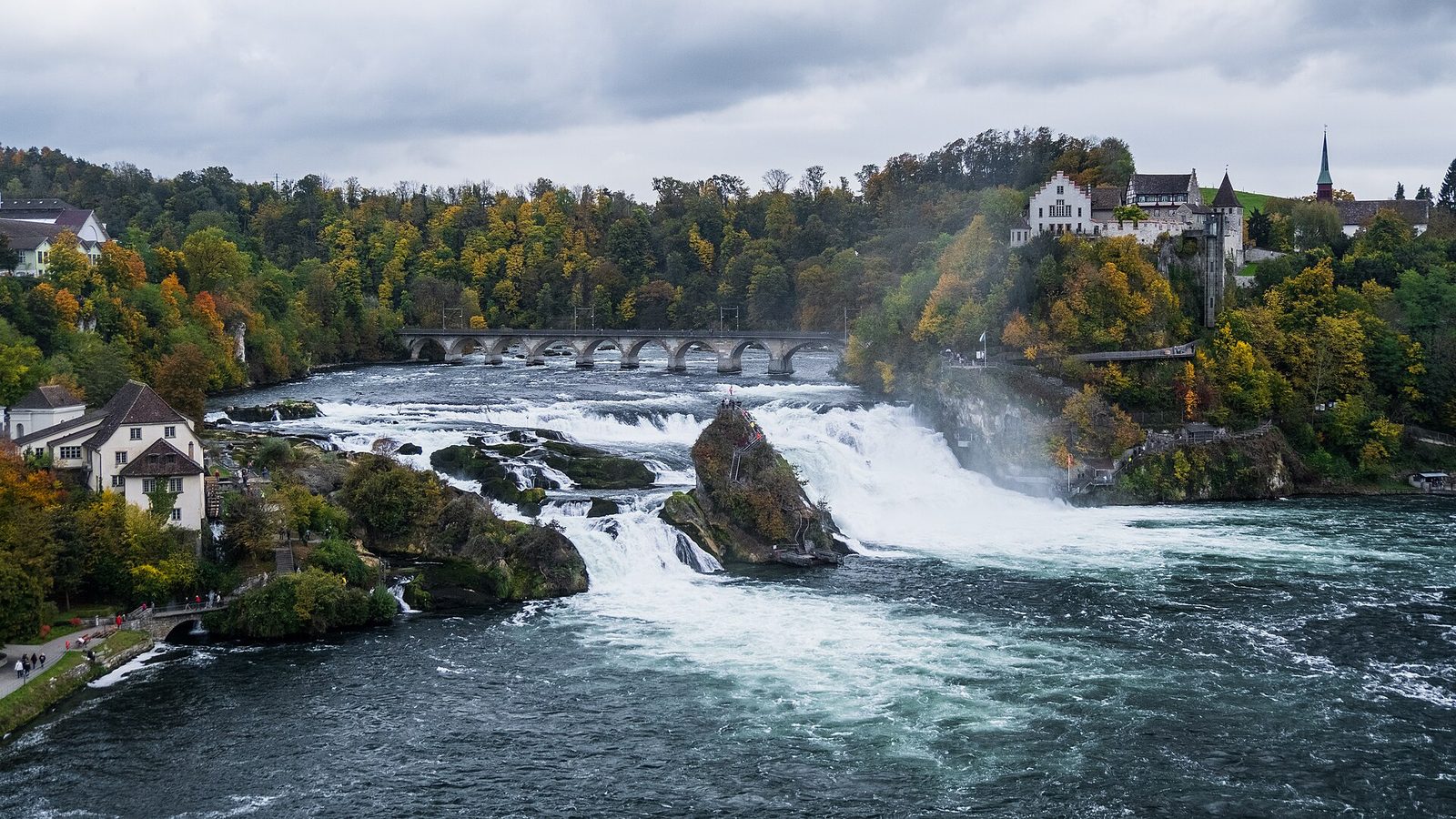 Switzerland sightseeing at the Rhine Falls: autumn trees, the arched railway bridge and stairs up the central rock