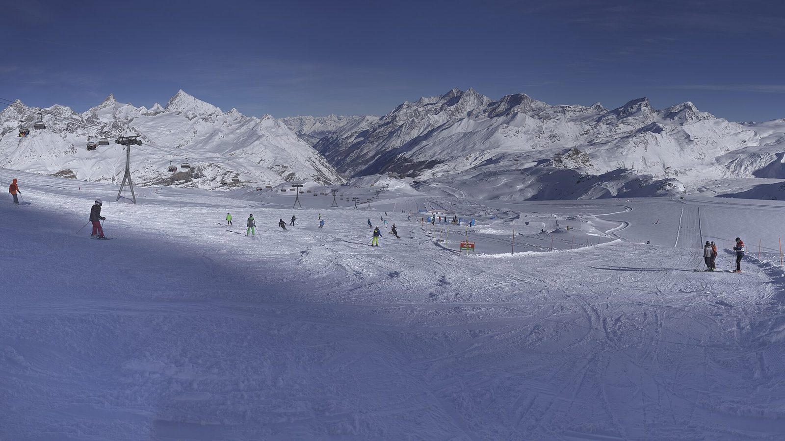 Switzerland sports in winter: skiers on a wide piste below chairlifts and snow-covered Alpine peaks