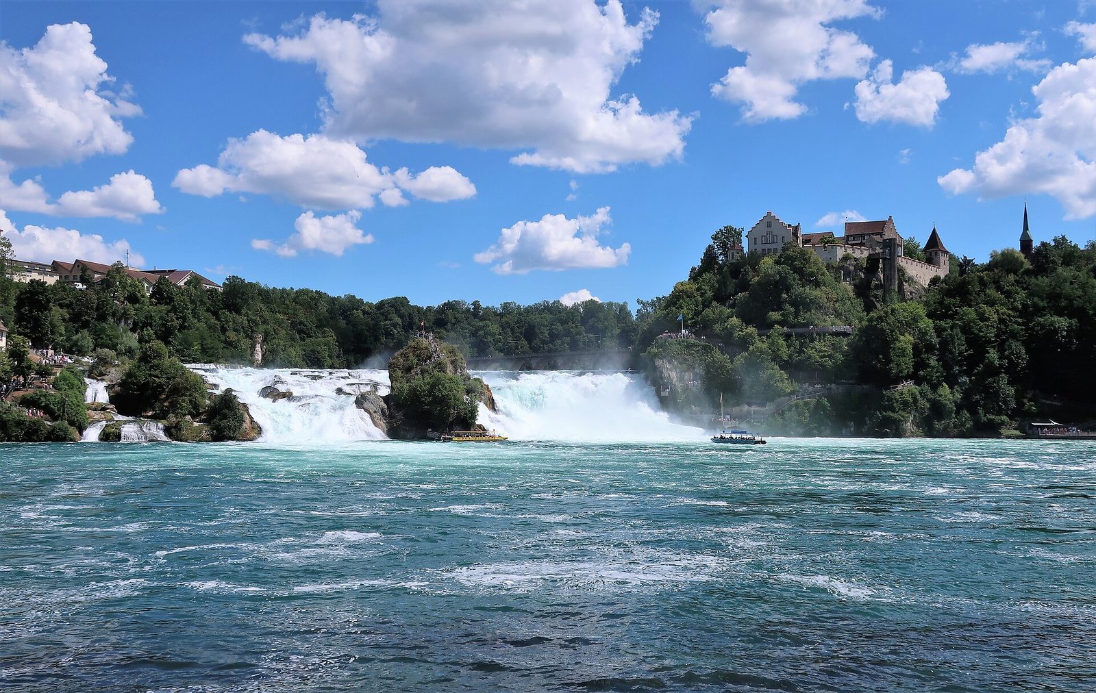 Things to do in Switzerland: the Rhine Falls with Laufen Castle on the wooded cliff and two boats near the rock