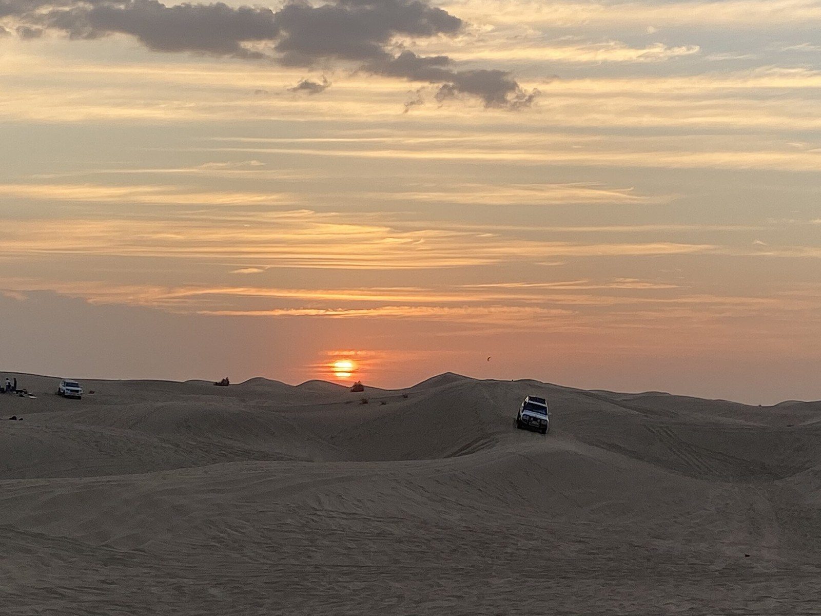 Top Dubai tours: four-wheel drives cross wide sand hills at sunset under streaks of orange cloud