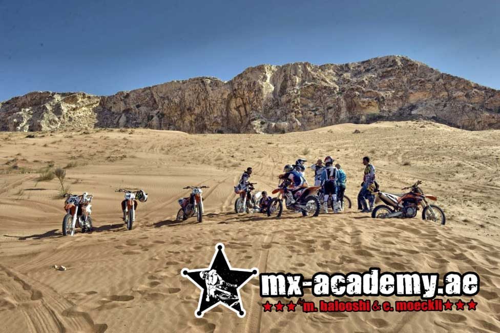 Top Dubai tours on two wheels: riders with their motorbikes gather on the sand below a rocky mountain ridge